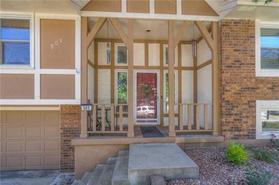 Doorway to property featuring a garage and covered porch, Teared stairs with landscaping. | Image 1