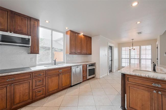 Stainless steel appliances, extensive cabinetry, and an abundance of natural light make this kitchen a standout. The blend of wood tones and sleek finishes creates a warm and modern culinary space. | Image 19