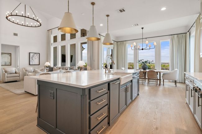Kitchen with a chandelier, decorative light fixtures, light wood-style flooring, a kitchen island with sink, and a towering ceiling | Image 14