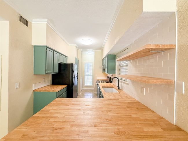Kitchen featuring green cabinetry, ornamental molding, open shelves, freestanding refrigerator, and wood counters | Image 8