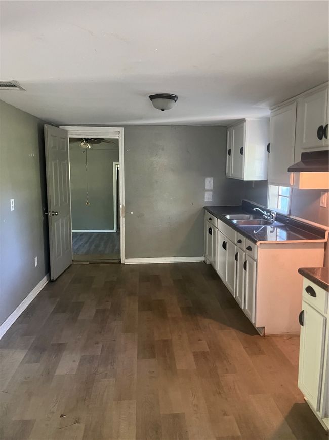 Kitchen with exhaust hood, visible vents, a sink, white cabinetry, and dark countertops | Image 6