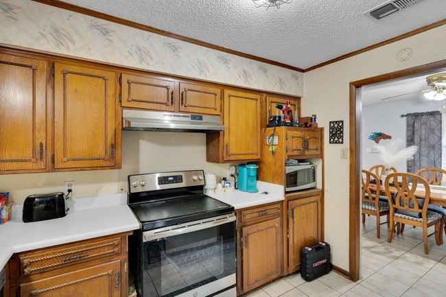 Kitchen with stainless steel appliances, under cabinet range hood, brown cabinetry, light countertops, and light tile patterned floors | Image 8