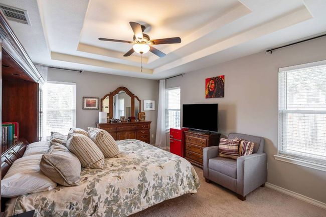 Bedroom featuring ceiling fan, light carpet, a tray ceiling, baseboards, and visible vents | Image 8