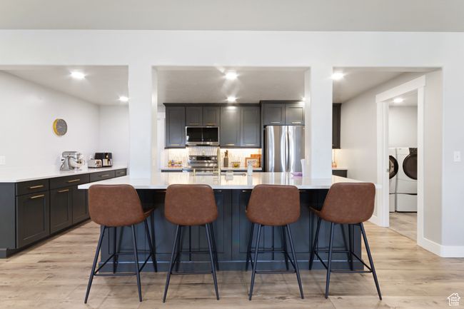Kitchen with light wood finished floors, light countertops, washer and dryer, tasteful backsplash, and appliances with stainless steel finishes | Image 21