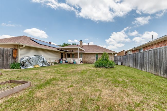 Rear view of house with solar panels, a vegetable garden, roof with shingles, brick siding, and a chimney | Image 12