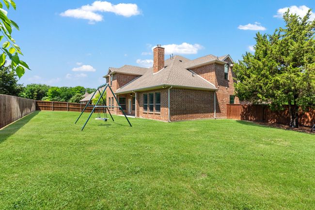 Rear view of house with a playground, a chimney, a fenced backyard, a yard, and brick siding | Image 40