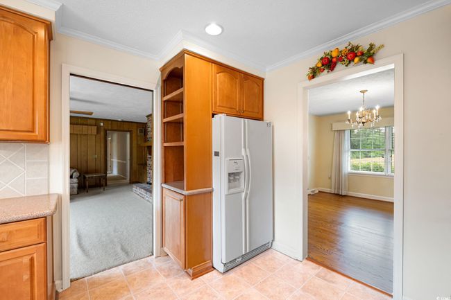 Kitchen featuring white refrigerator with ice dispenser, crown molding, a chandelier, baseboards, and light tile patterned floors | Image 11
