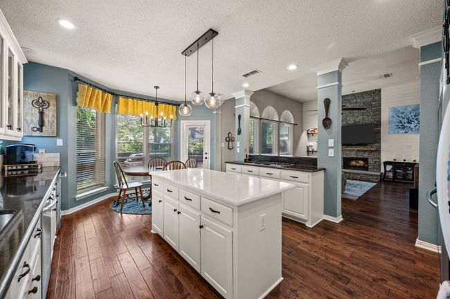 Kitchen featuring white cabinetry, a kitchen island, hanging light fixtures, dark wood finished floors, and a fireplace | Image 16