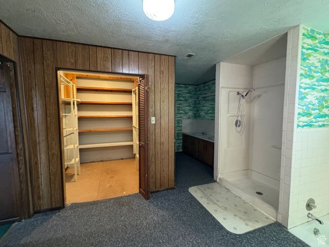 Full bathroom with a shower, a textured ceiling, a closet, and wooden walls | Image 13