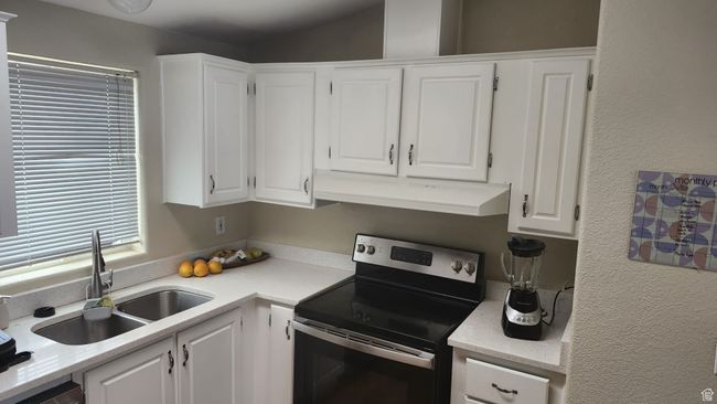 Kitchen featuring stainless steel appliances, a sink, under cabinet range hood, white cabinetry, and light countertops | Image 12