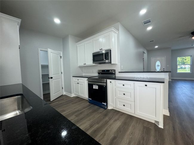 Kitchen featuring range with electric stovetop, stainless steel microwave, dark wood-style flooring, white cabinetry, and recessed lighting | Image 8