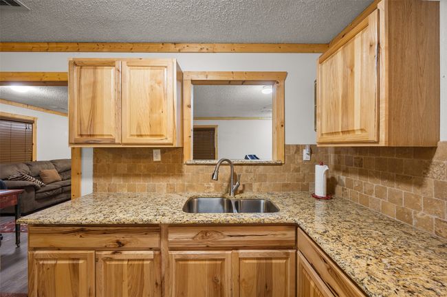 Kitchen with a sink, decorative backsplash, light stone counters, a textured ceiling, and light brown cabinets | Image 20