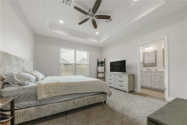 Bedroom with a raised ceiling, connected bathroom, recessed lighting, light carpet, and ceiling fan | Image 6