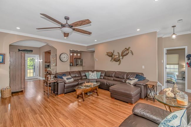 Living area with a ceiling fan, plenty of natural light, arched walkways, light wood-type flooring, and crown molding | Image 13