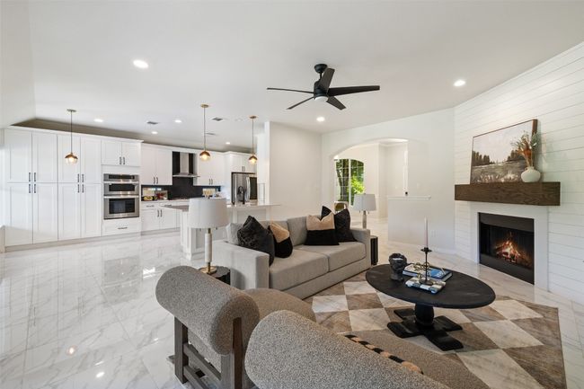 Living area with light marble finish flooring, arched walkways, recessed lighting, a large fireplace, and a ceiling fan | Image 15
