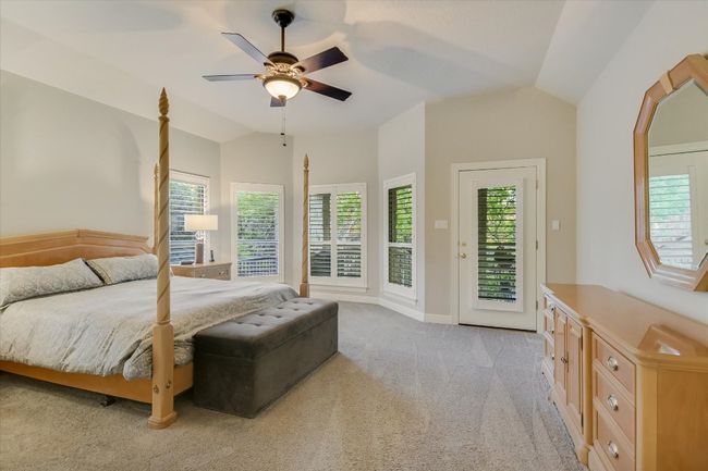 Primary bedroom with ceiling fan, baseboards, vaulted ceiling, light carpet, and access to outside | Image 11