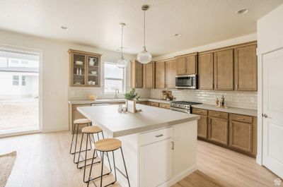 Kitchen with tasteful backsplash, light wood-type flooring, pendant lighting, a center island, and appliances with stainless steel finishes | Image 2