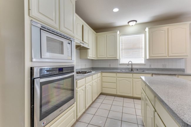 Kitchen featuring backsplash, light tile patterned floors, a sink, and white appliances | Image 13