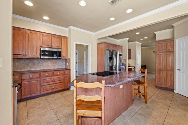 Kitchen featuring brown cabinetry, a kitchen island, light tile patterned flooring, stainless steel appliances, and a kitchen breakfast bar | Image 13