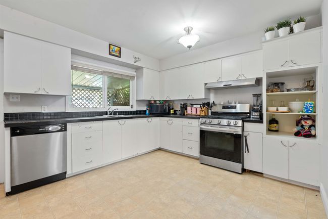 Kitchen featuring dark countertops, under cabinet range hood, white cabinetry, and appliances with stainless steel finishes | Image 7