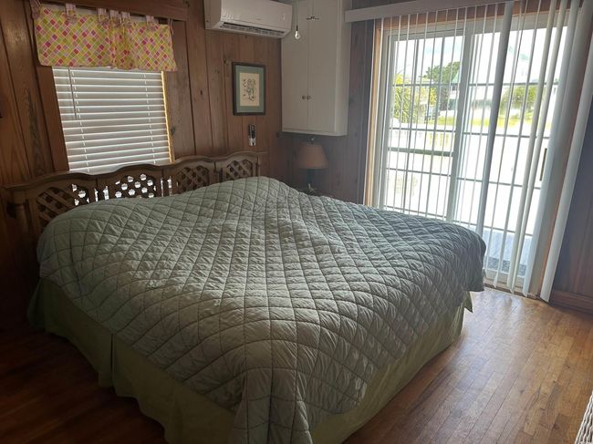 Bedroom with a wall unit AC, hardwood / wood-style flooring, multiple windows, and wooden walls | Image 20