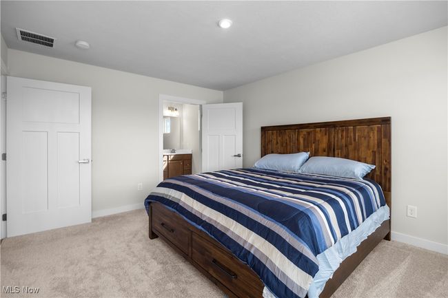Bedroom featuring visible vents, baseboards, ensuite bathroom, and light carpet | Image 24