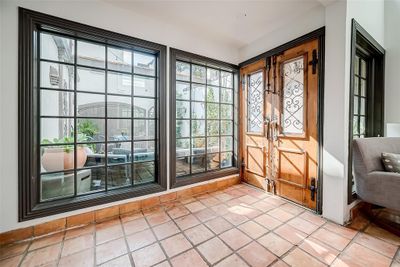 This entry features elegant Saltillo tile flooring and large black-framed windows providing ample natural light. Antique French Doors with windows featuring wrought iron panels lead to the front courtyard. | Image 3