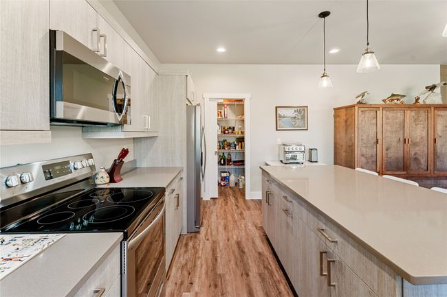 Kitchen with appliances with stainless steel finishes, light wood-type flooring, light countertops, hanging light fixtures, and a kitchen island | Image 12