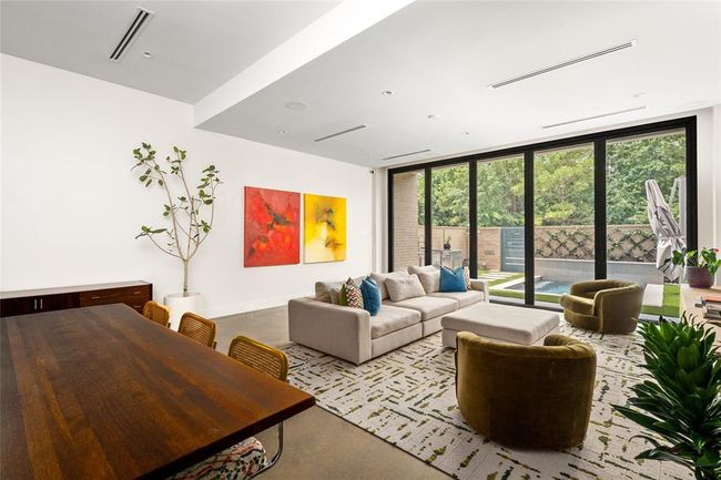 This light-filled living and dining area embraces a modern yet inviting aesthetic, with clean lines and polished concrete floors. A wall of Ram sliding glass doors opens to the private courtyard, seamlessly connecting the interior to serene, tree-lined views and the nearby expanse of Memorial Park—perfect for relaxed living and easy entertaining. | Image 9