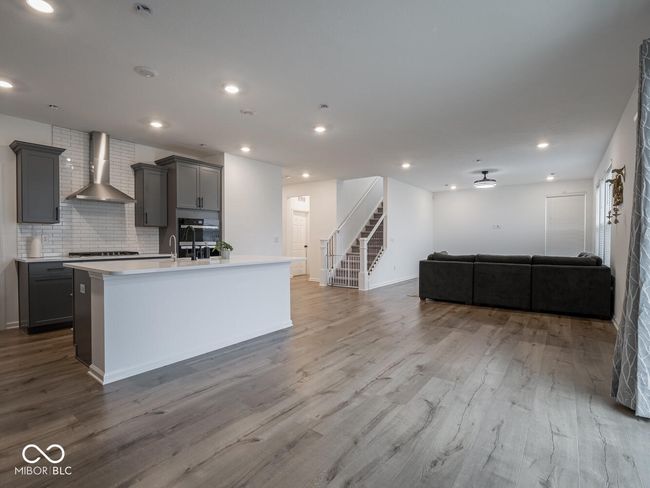 kitchen featuring open floor plan, wall chimney range hood, an island with sink, wood finished floors, and gray cabinets | Image 14