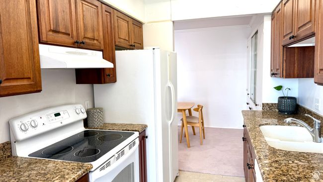 Kitchen with white range with electric stovetop, under cabinet range hood, ornamental molding, brown cabinets, and light colored carpet | Image 32