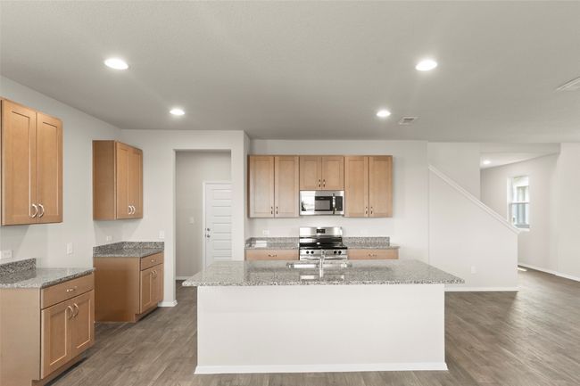 Kitchen featuring appliances with stainless steel finishes, wood finished floors, a kitchen island with sink, recessed lighting, and light stone countertops | Image 17