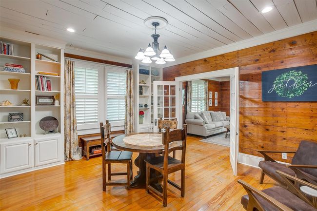 Dining room featuring light wood-type flooring, a chandelier, wooden walls, crown molding, and built in shelves | Image 15