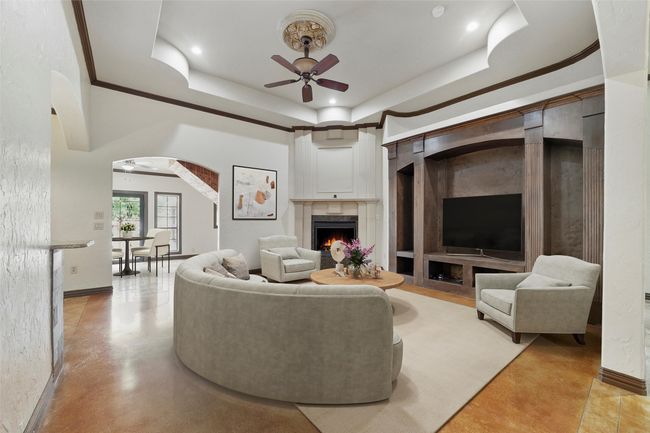 Living area featuring ceiling fan, a raised ceiling, a premium fireplace, baseboards, and arched walkways | Image 8