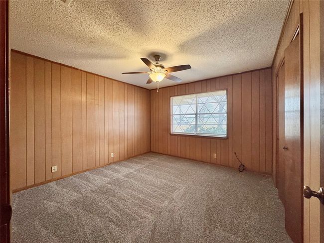 Empty room with a textured ceiling, wooden walls, ceiling fan, and carpet flooring | Image 19