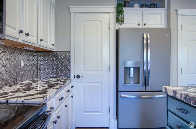 Kitchen featuring backsplash, light stone countertops, stainless steel refrigerator with ice dispenser, and white cabinetry | Image 10