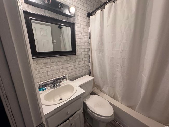 Full bathroom featuring brick wall, shower / bathtub combination with curtain, toilet, and vanity | Image 7