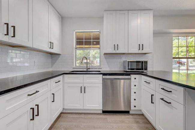 Kitchen with appliances with stainless steel finishes, a sink, white cabinets, light wood-type flooring, and backsplash | Image 8