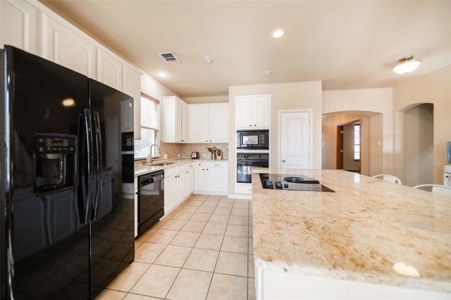 Kitchen featuring black appliances, arched walkways, light tile patterned flooring, backsplash, and light stone countertops | Image 10