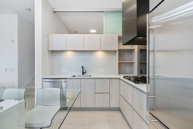 Kitchen featuring light countertops, a sink, appliances with stainless steel finishes, modern cabinets, and wall chimney range hood | Image 11