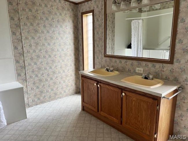 Full bath with double vanity, wallpapered walls, tile patterned floors, and a shower with shower curtain | Image 4