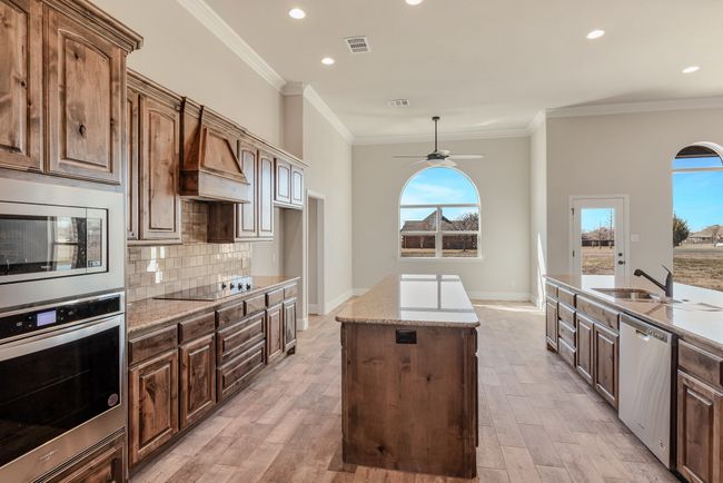Kitchen featuring stainless steel appliances, a kitchen island, premium range hood, a ceiling fan, and light stone countertops | Image 8