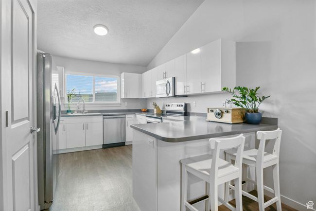 Kitchen featuring vaulted ceiling, light wood finished floors, a peninsula, stainless steel appliances, and white cabinets | Image 13