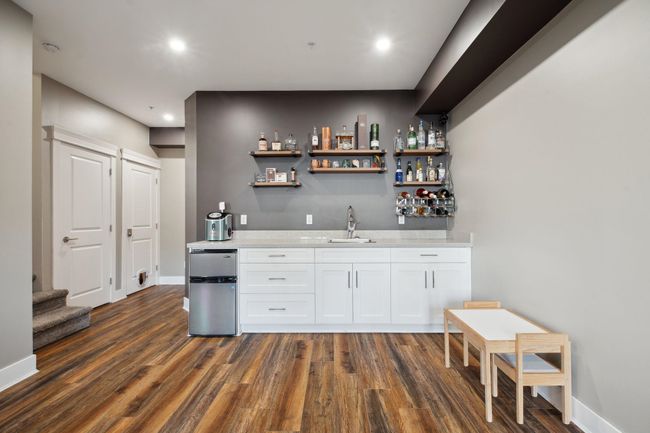 Bar with dark wood-type flooring, wet bar, a sink, stairs, and baseboards | Image 31
