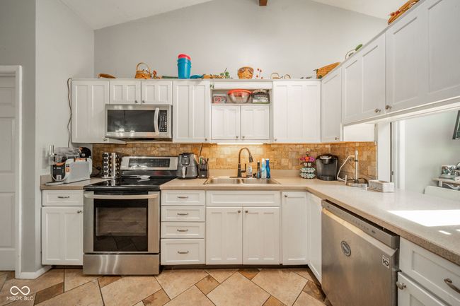 kitchen featuring stainless steel appliances, decorative backsplash, light countertops, white cabinets, and lofted ceiling | Image 15