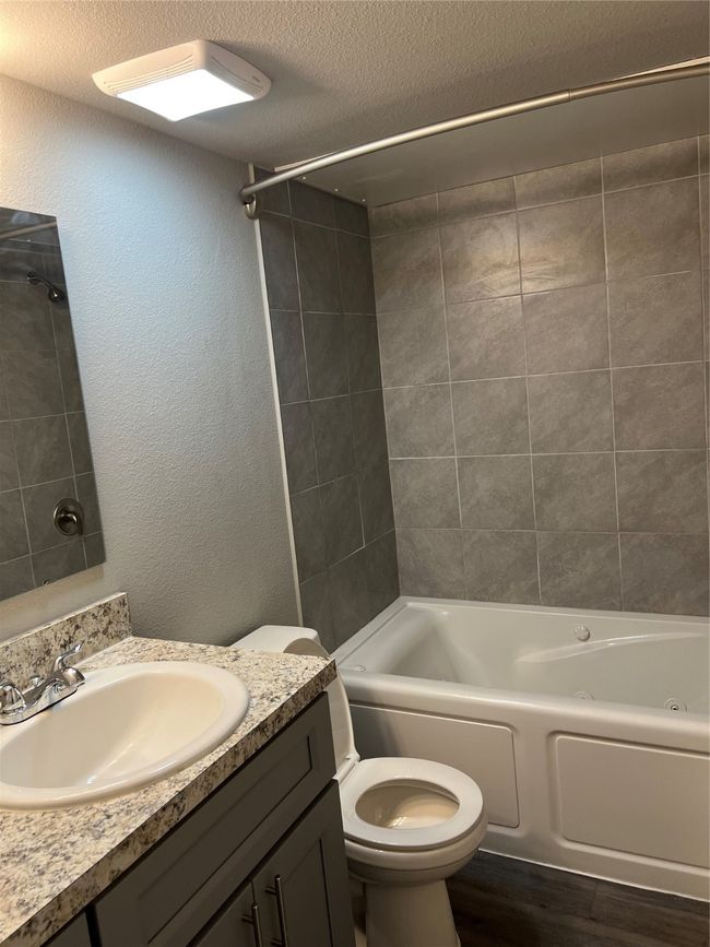 Full bath featuring vanity, wood finished floors, shower / tub combination, toilet, and a textured ceiling | Image 8