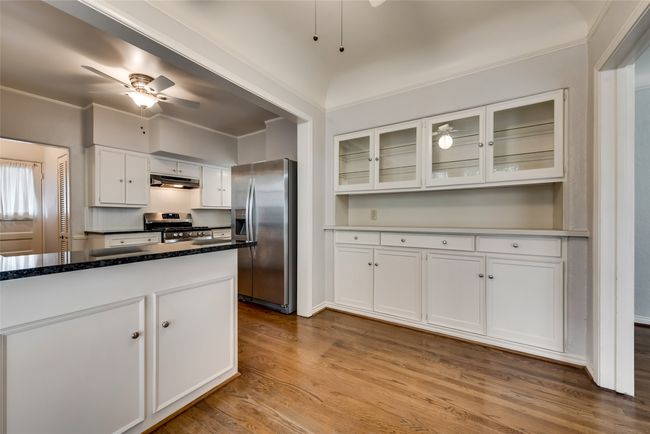 Kitchen with stainless steel appliances, under cabinet range hood, white cabinets, wood finished floors, and a ceiling fan | Image 12
