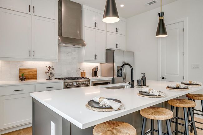 Kitchen featuring visible vents, backsplash, wall chimney range hood, stainless steel appliances, and an island with sink | Image 5