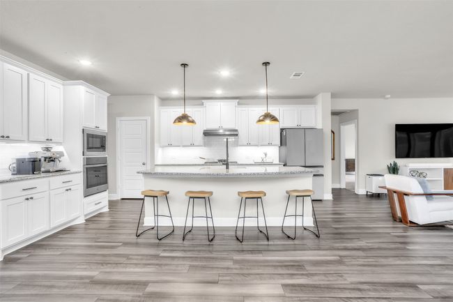 Kitchen featuring under cabinet range hood, an island with sink, decorative backsplash, appliances with stainless steel finishes, and white cabinets | Image 5