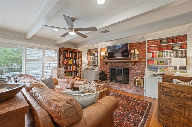 Living area featuring beamed ceiling, ceiling fan, a brick fireplace, wood finished floors, and built in features | Image 14